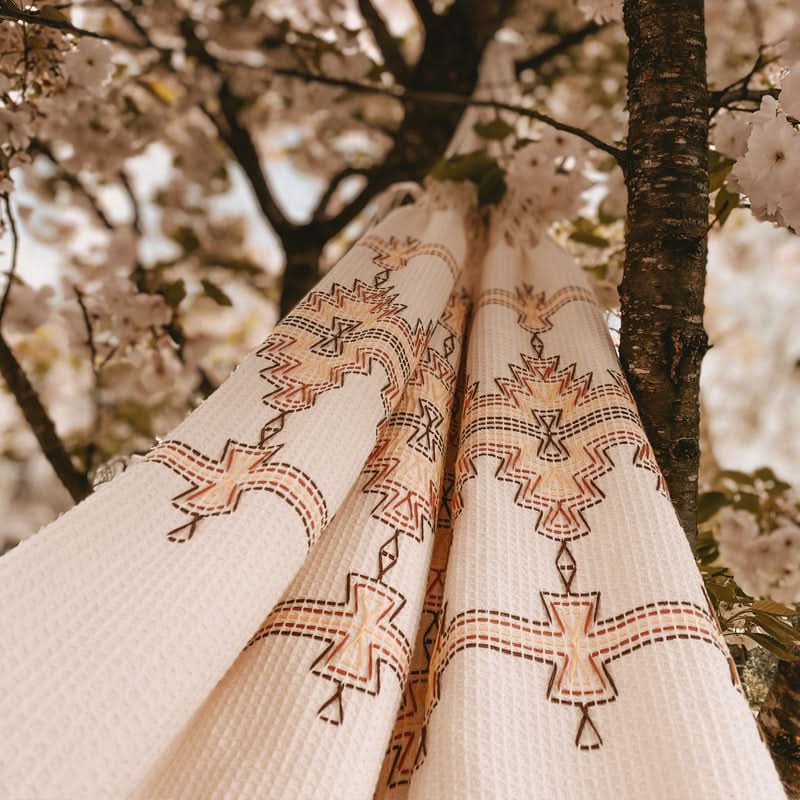Decorative fabric with tribal patterns hanging against a natural background with trees and flowers.