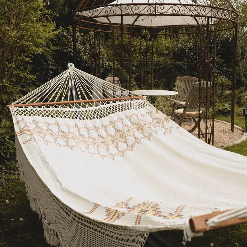 White hammock with intricate patterns in a garden setting with a gazebo and chairs.
