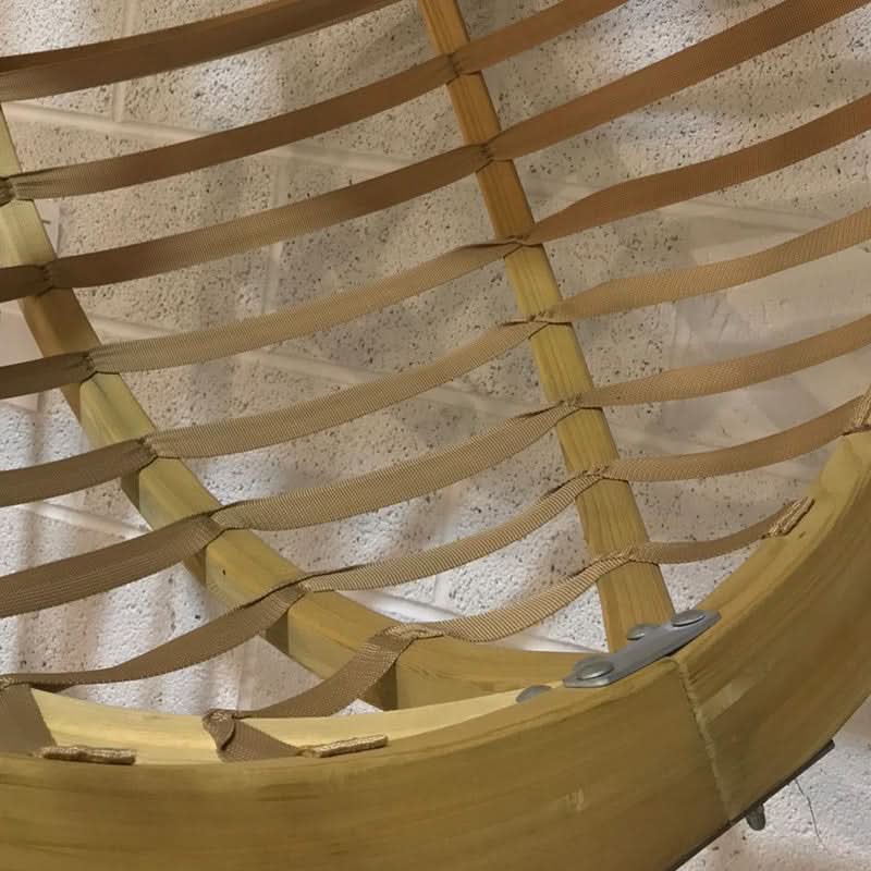 Close-up of a woven chair with wooden frame and straps on a textured surface.