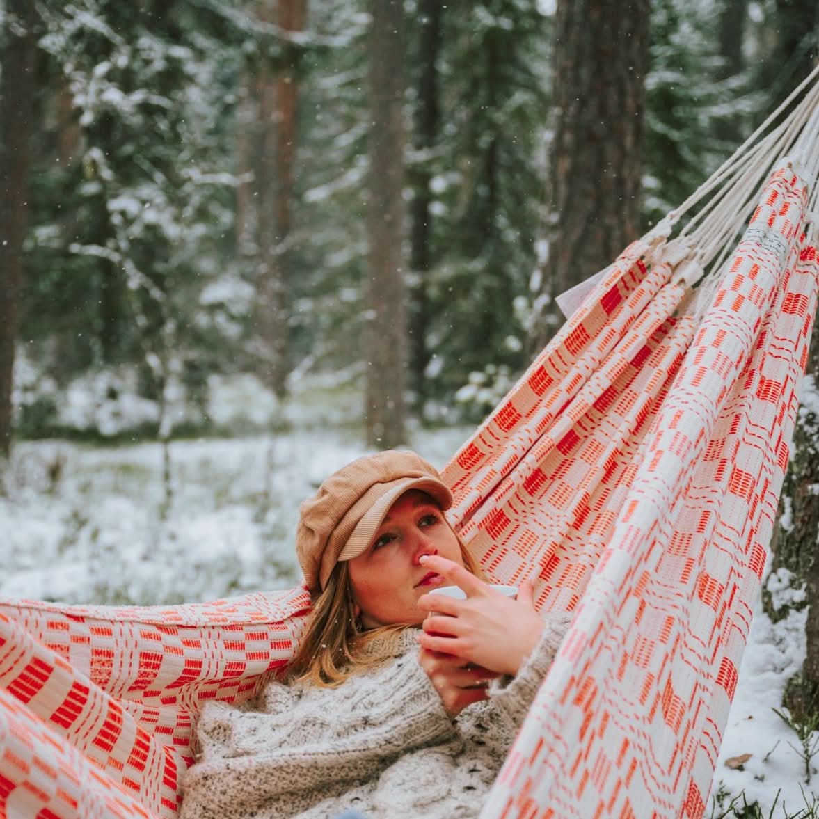Person lying in a red and white patterned hammock in a snowy forest.
