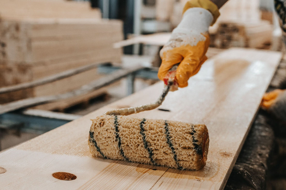 Person applying wood finish to a wooden surface using a roller.