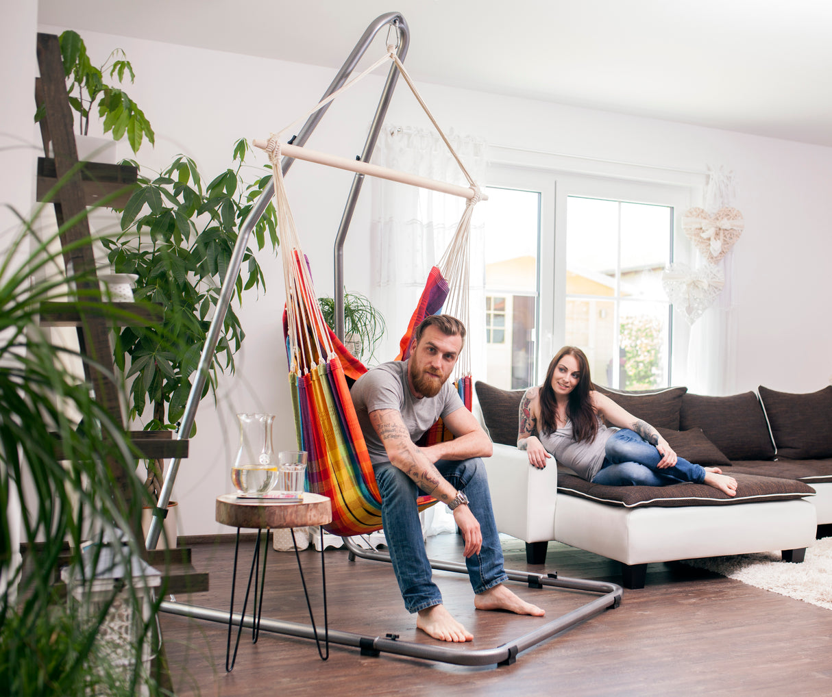 Two people are using a hanging chair in a modern living room.