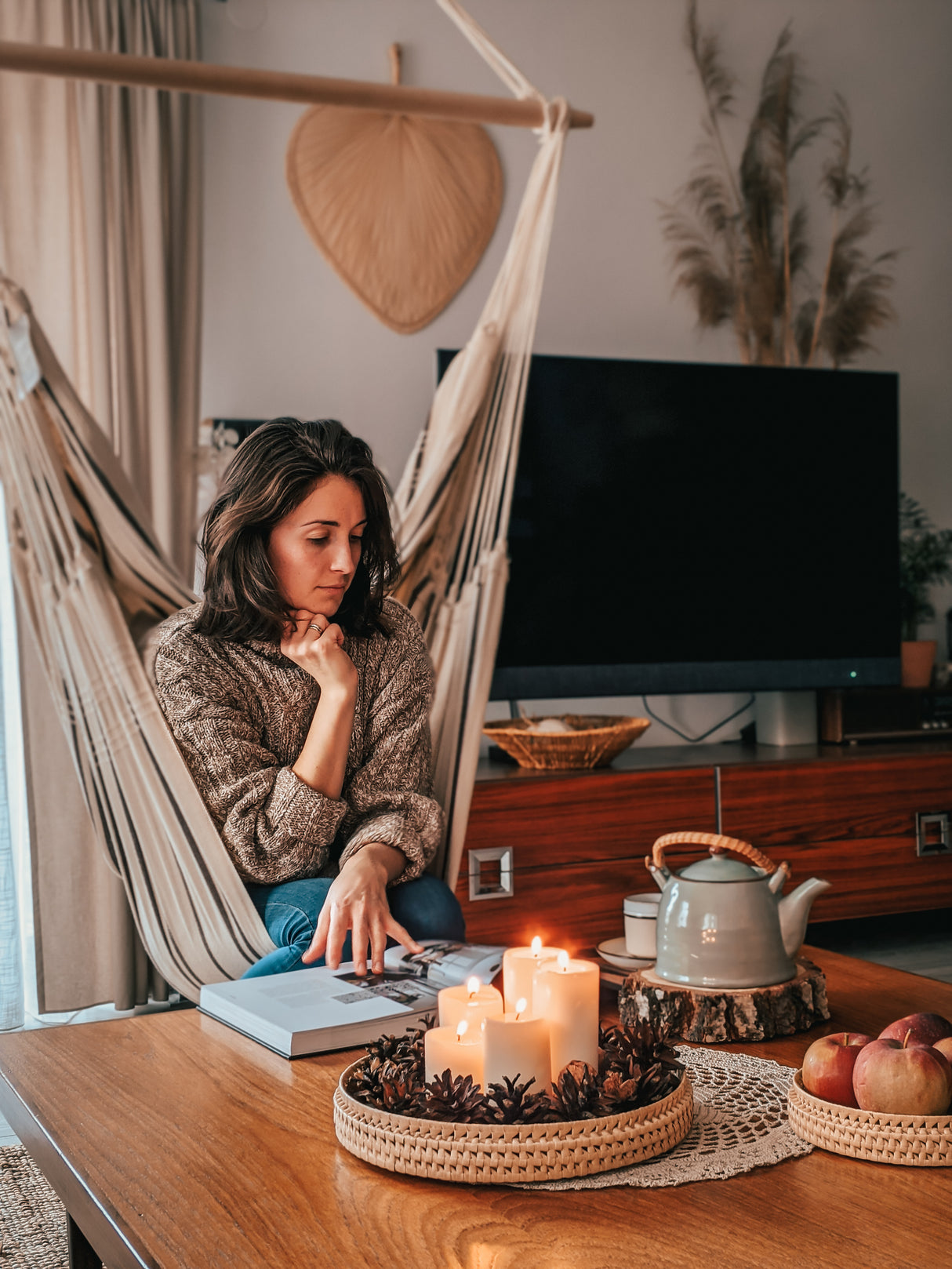 A woman sitting in a hammock in a cosy living room with candles and a teapot.