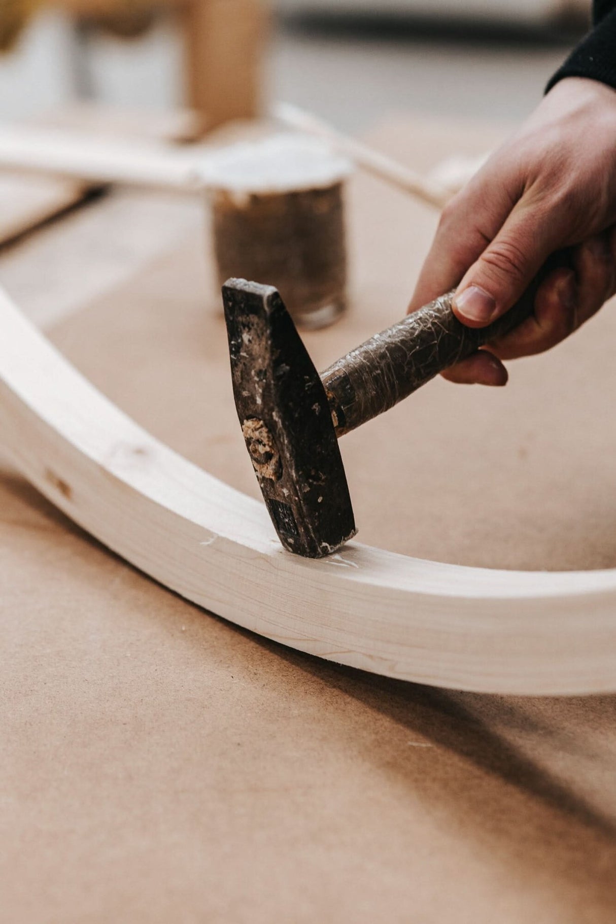 Hand using a hammer on a wooden chair rim.