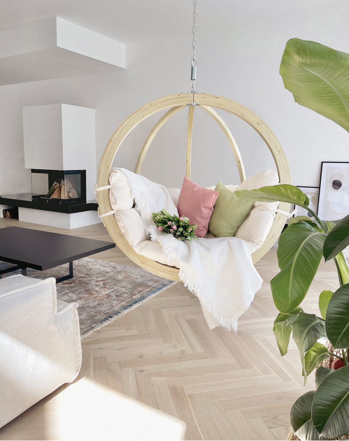 Hanging chair in a modern living room with plants and a fireplace.
