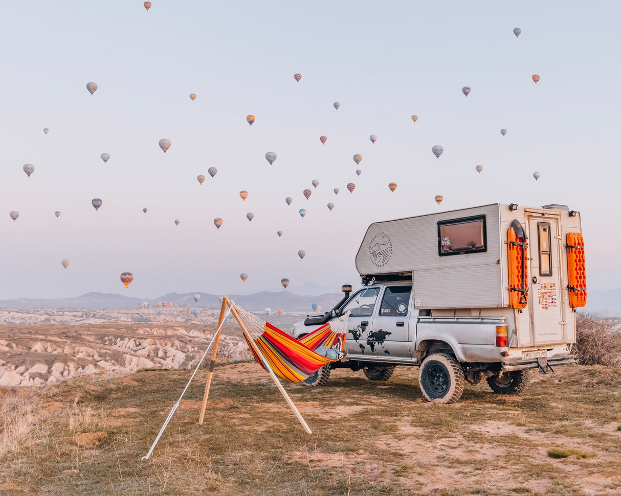Camper van with a hammock under hot air balloons in a scenic landscape