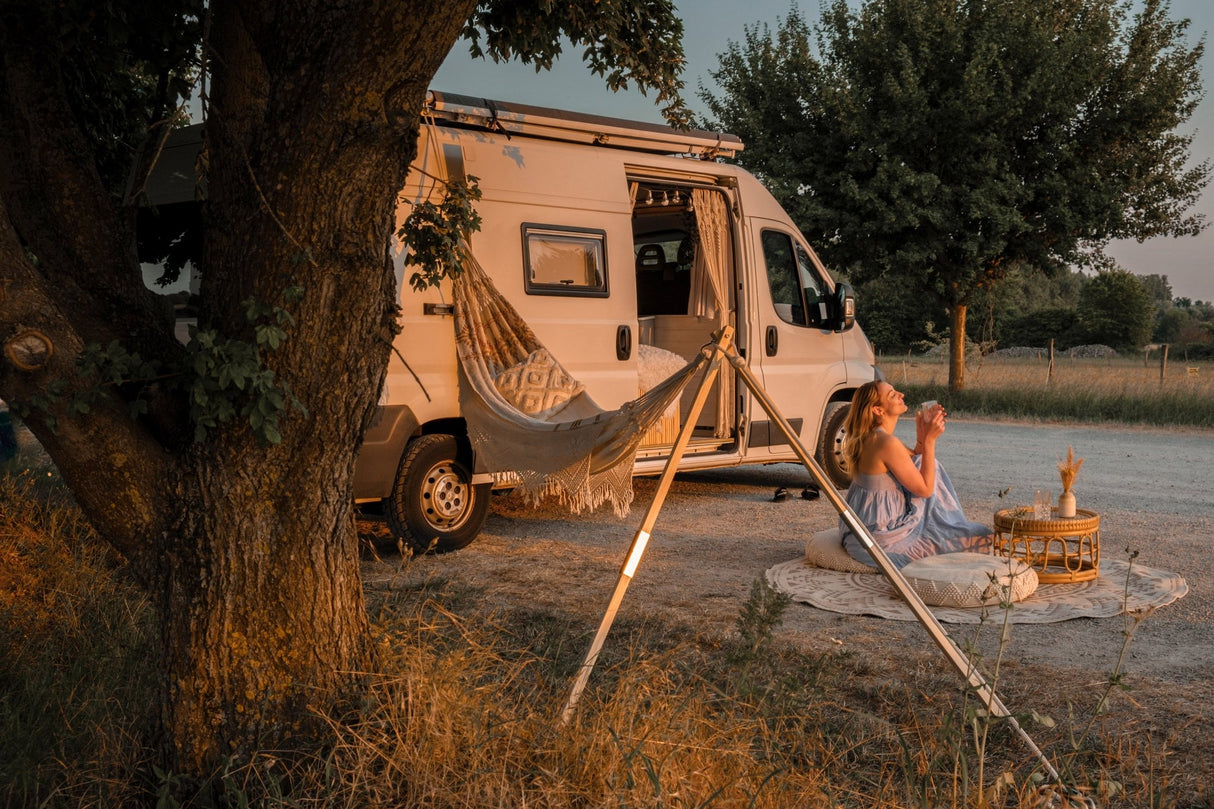 A person sitting by a van with a hammock near the Road