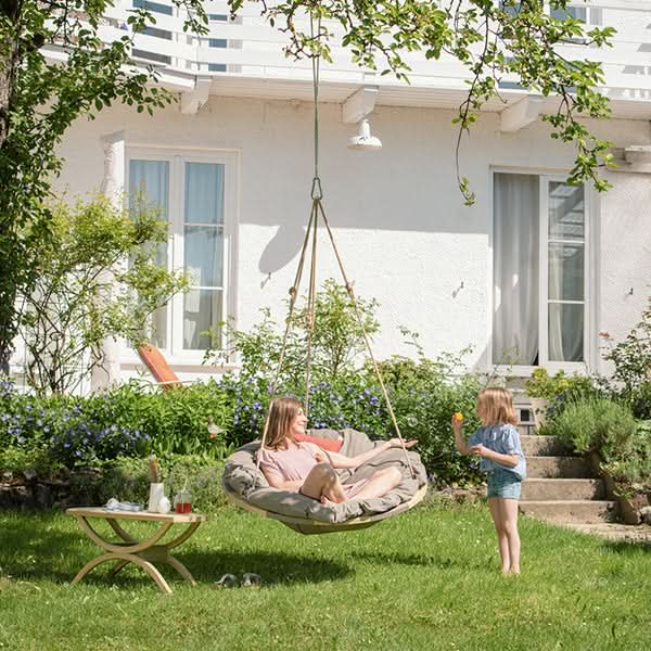 Two people in a hanging chair in a garden with a house in the background