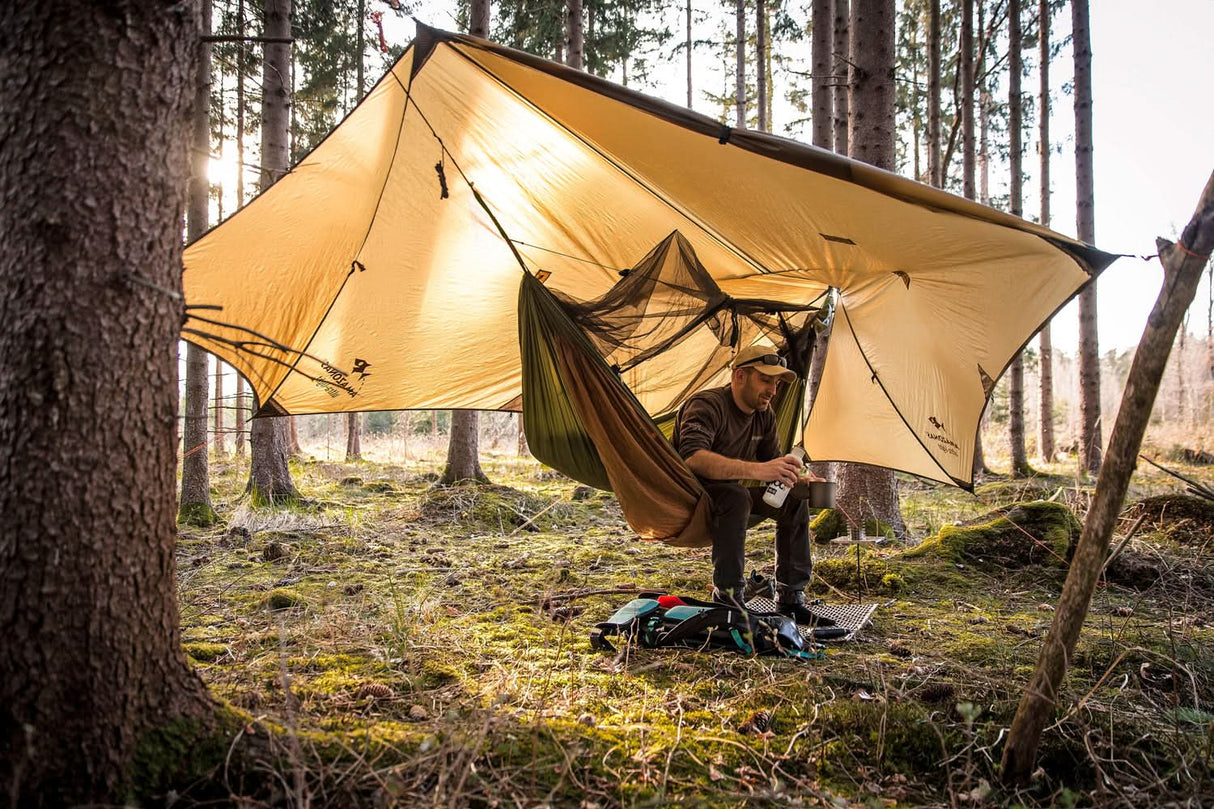 Person camping in a forest with a tent and hammock setup.