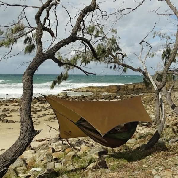 Brown hammock hanging between two trees on a rocky beach with ocean in the background