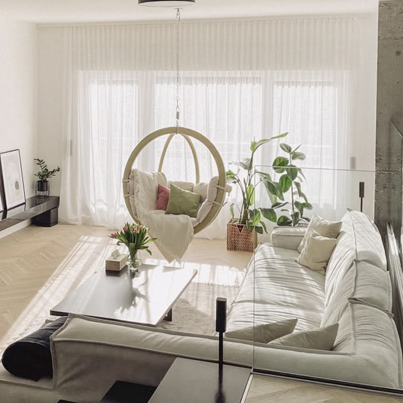 Modern living room with a white sofa, glass coffee table, and hanging chair.