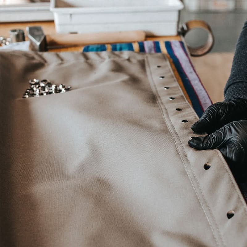 Person wearing black gloves working on a leather product with tools in the background