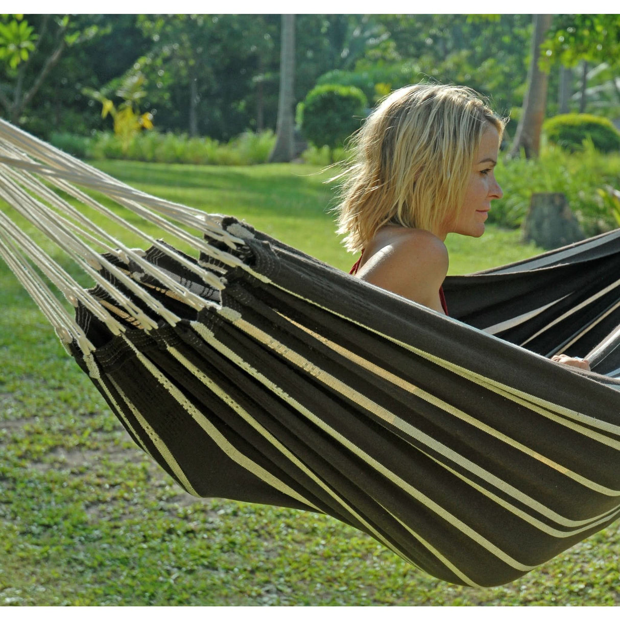 Woman relaxing in a striped hammock in a lush green outdoor setting
