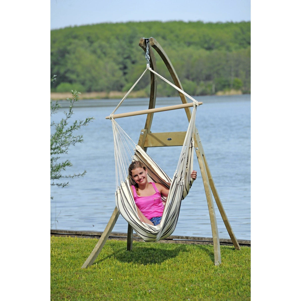 A person sitting in a hammock by a lake with a wooden stand