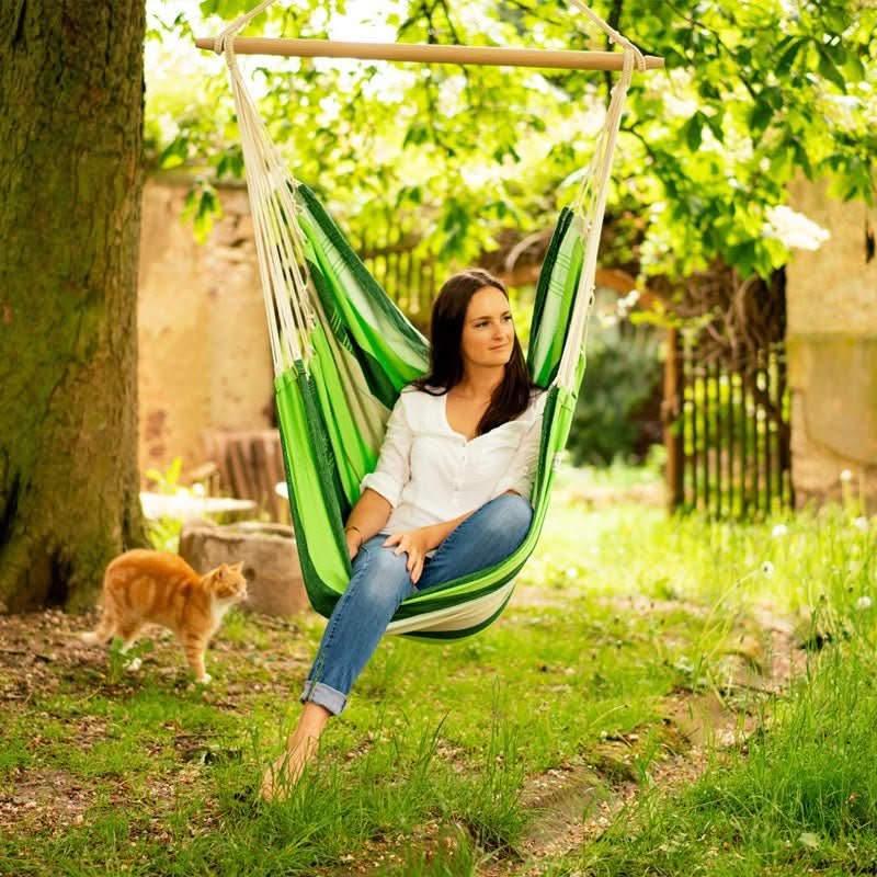 Woman sitting in a green hammock chair in a garden with a cat nearby