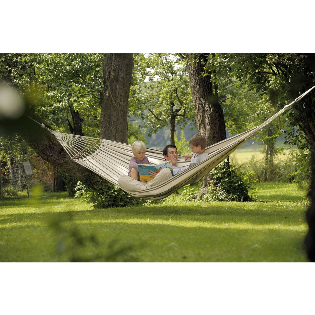 Two adults and two children in a hammock in a park setting