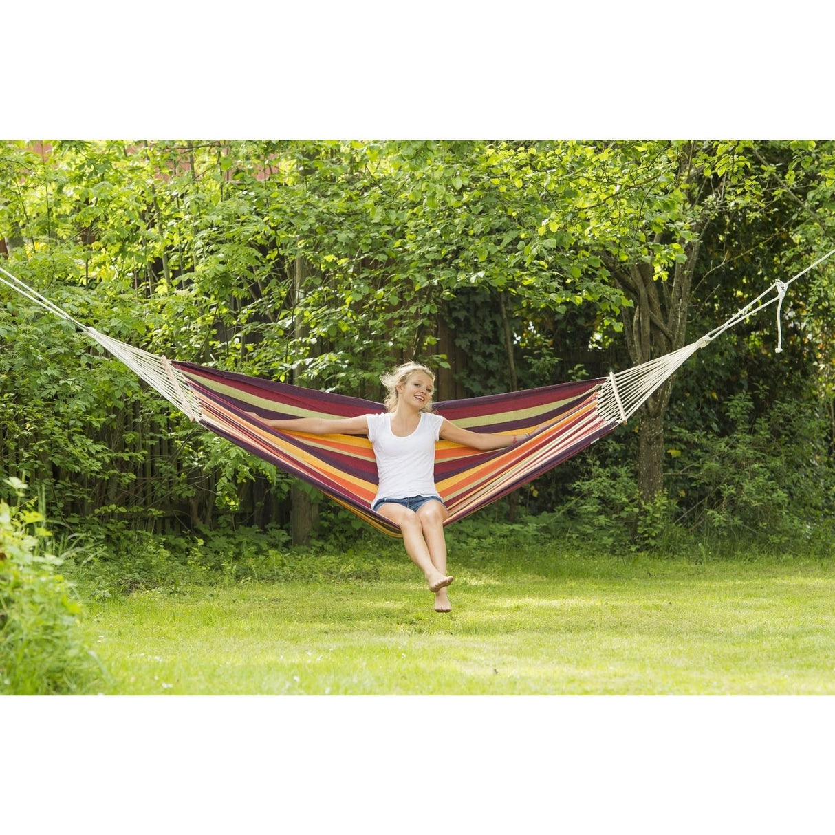 Woman sitting in a colourful hammock surrounded by greenery