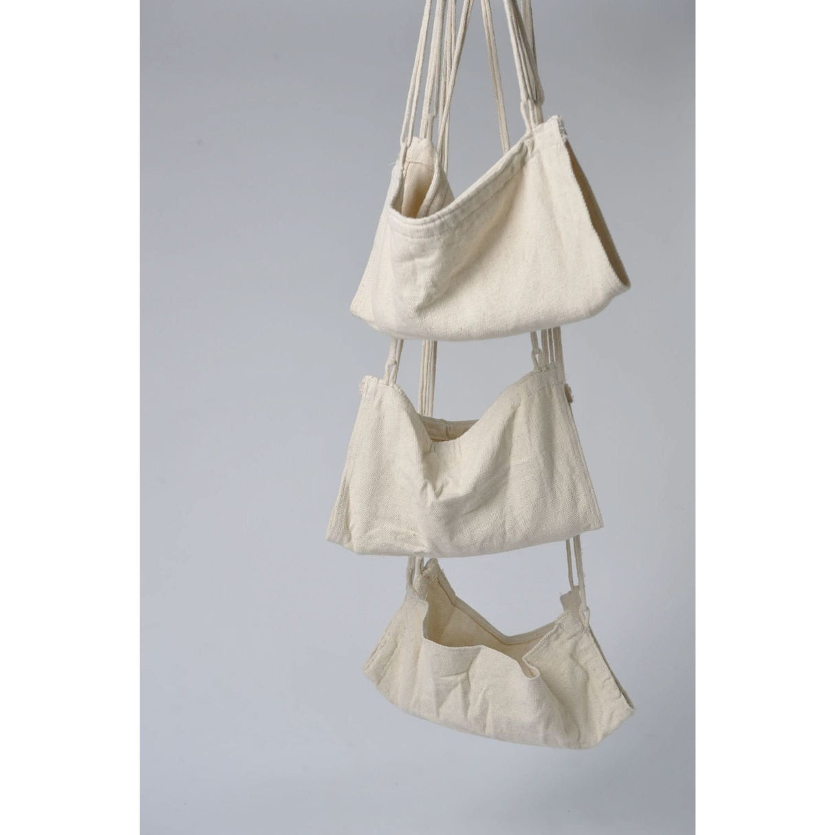 Three beige handbags of different sizes hanging against a light grey background