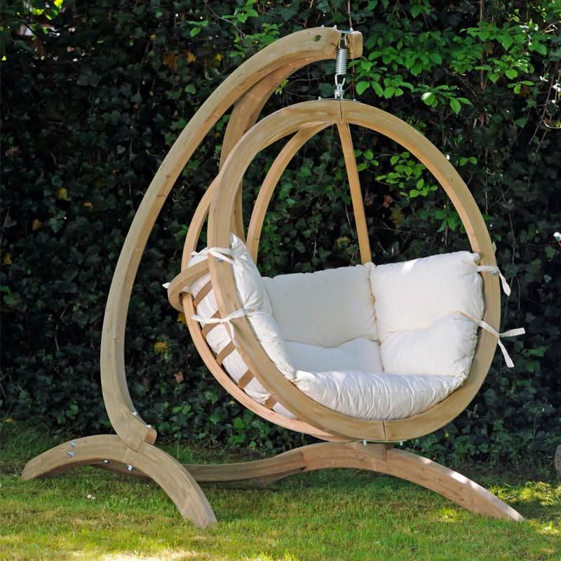 Hanging chair with white cushions on a wooden stand in an outdoor setting.