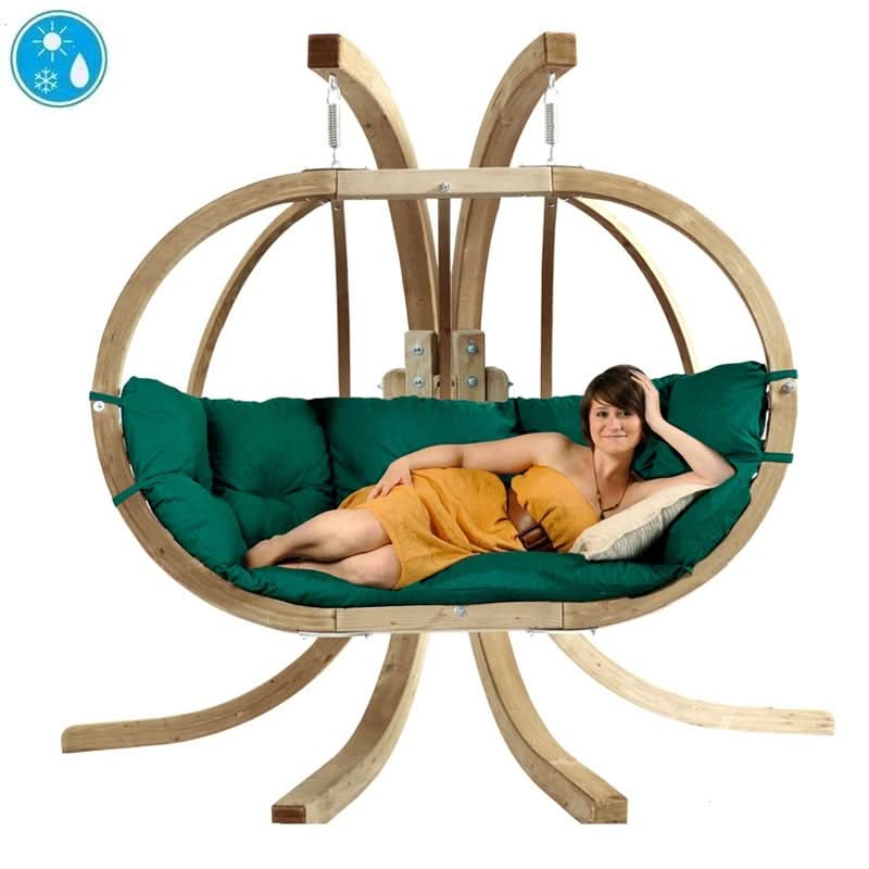 Person relaxing in a hanging egg chair with green cushions and a wooden frame.