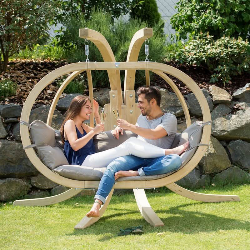 Two people are sitting in a wooden hanging chair outdoors.
