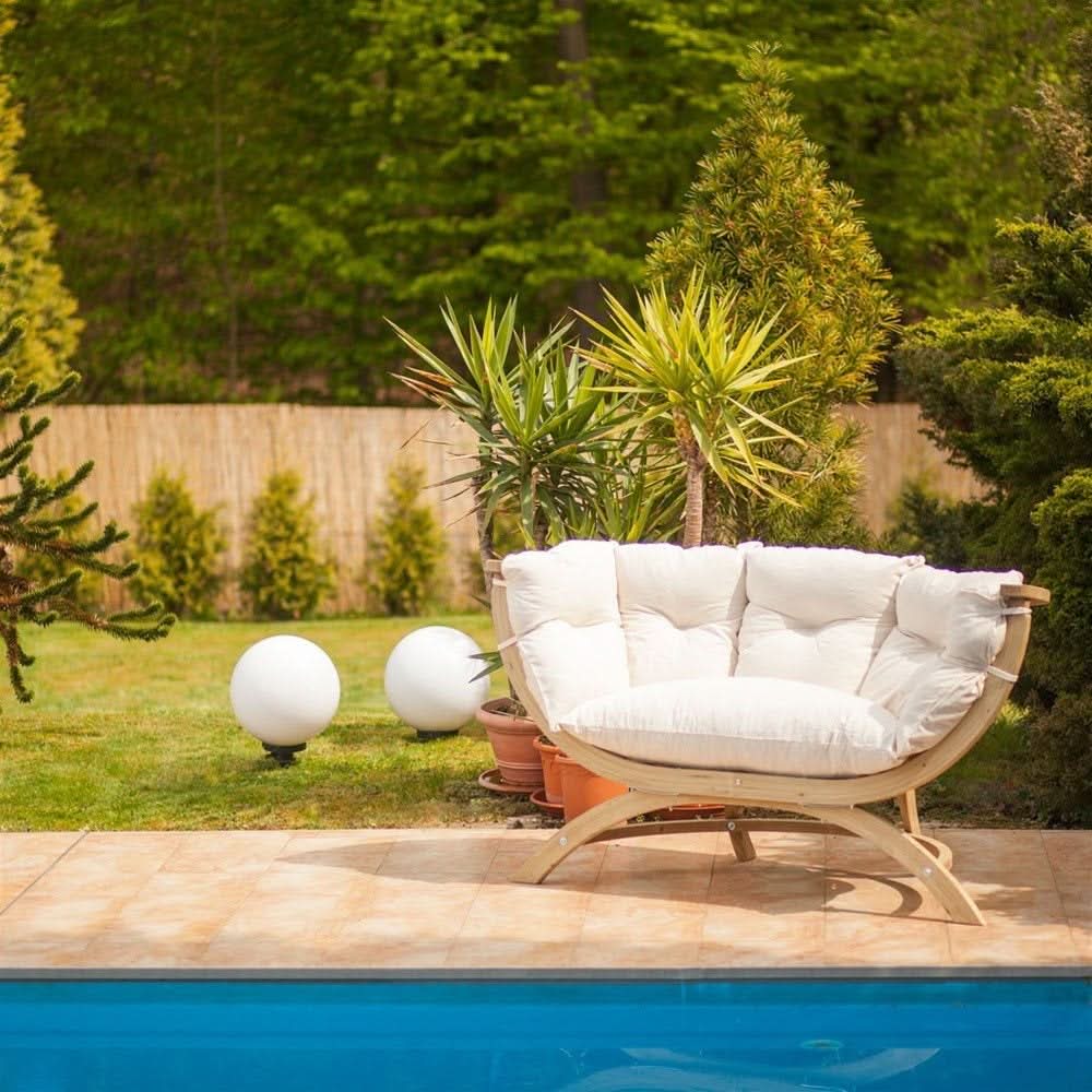 White cushioned outdoor chair by a pool with greenery in the background