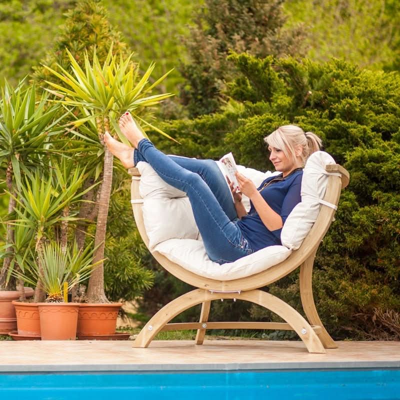 Woman relaxing in a modern chair by a pool with greenery in the background