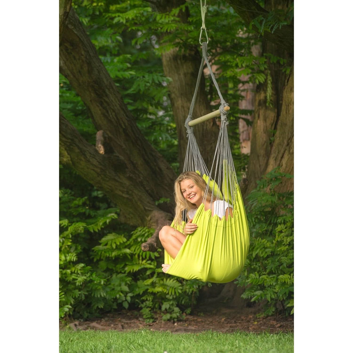 A person sitting in a bright green hammock swing surrounded by trees and greenery.