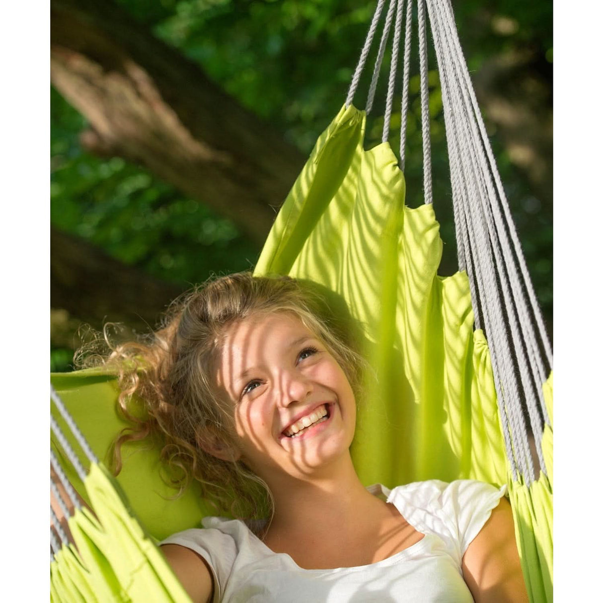 Child smiling in a green hammock with a natural background