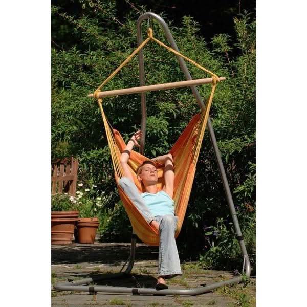 Person relaxing in an orange hammock chair with a stand in a garden setting.