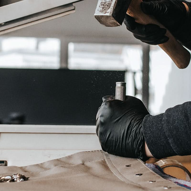 A person wearing black gloves is using a tool on a vehicle's undercarriage.