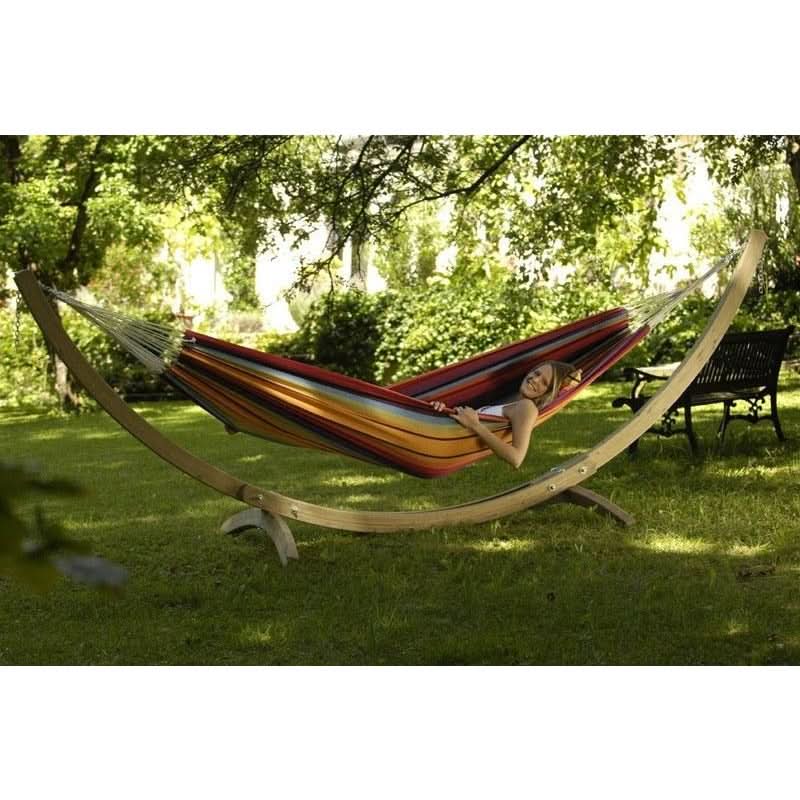 Person relaxing in a colourful hammock with a wooden stand in a garden setting.