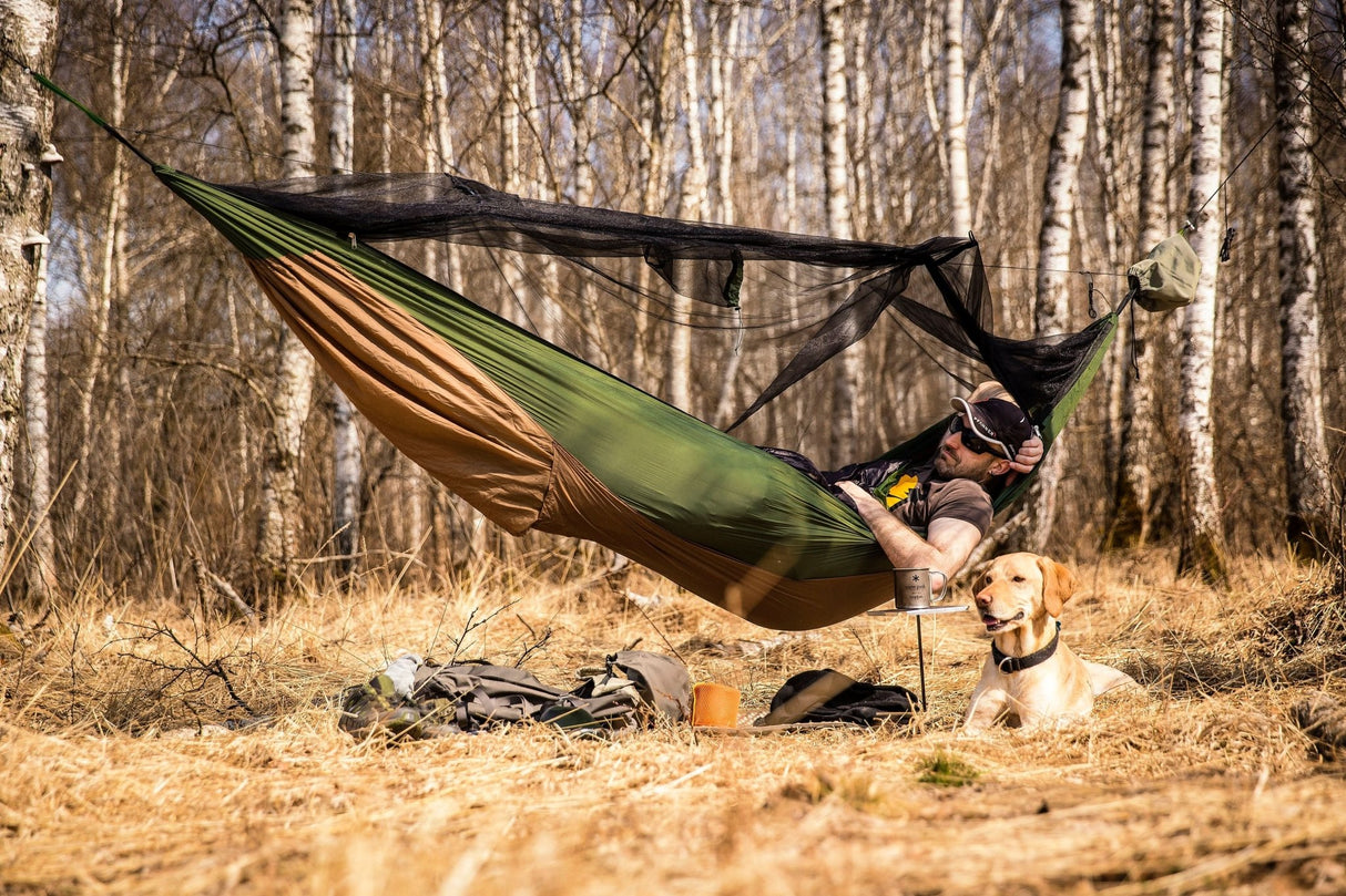 Person relaxing in a hammock with a dog in a forest setting