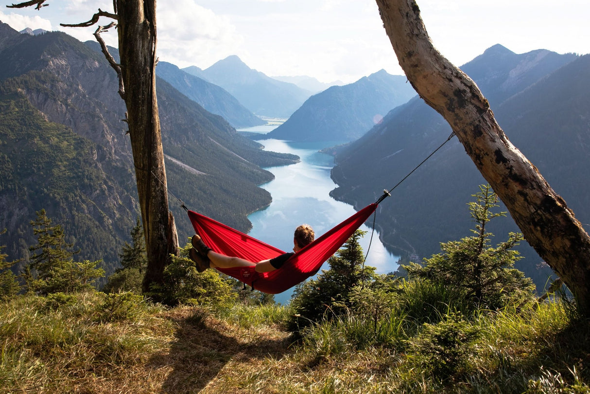 Person in a red hammock overlooking a scenic mountain landscape with a lake.