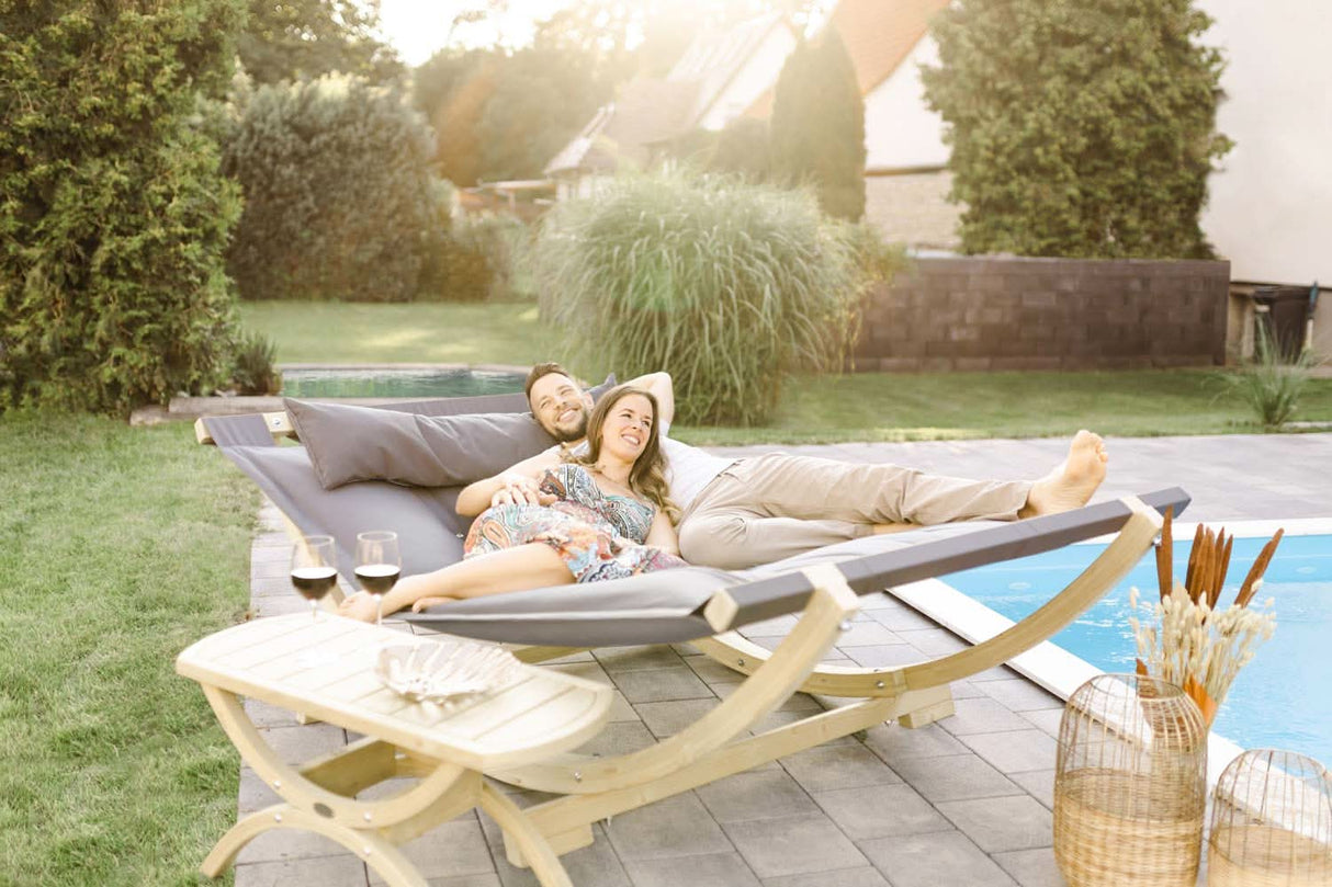 Two women relaxing on a lounge chair by a pool with a scenic garden view.