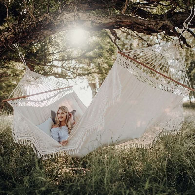 Person in a white hammock with tassels in a natural setting