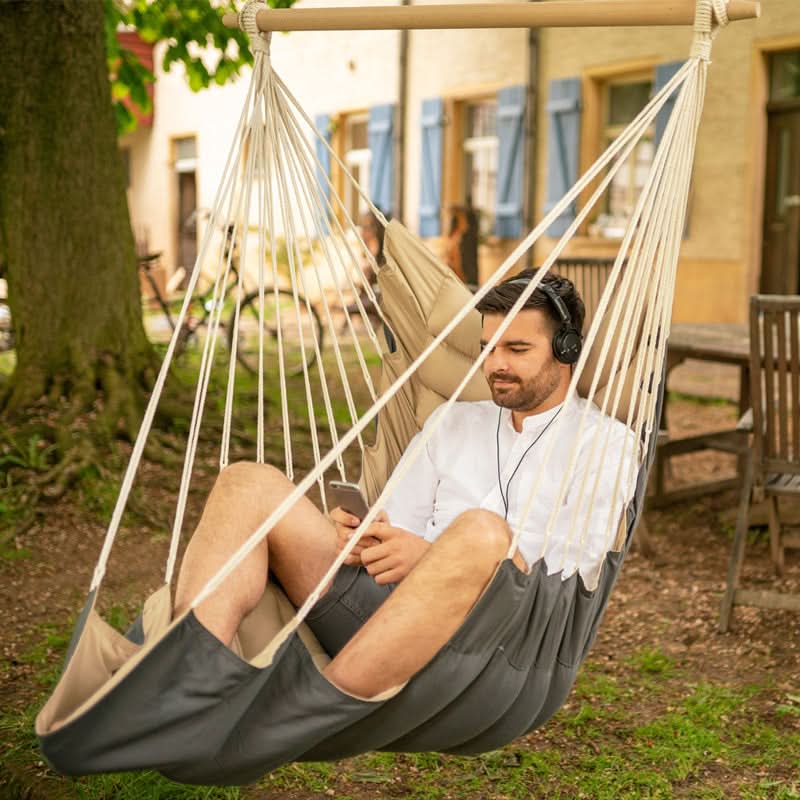 Man relaxing in a hammock outdoors, listening to music on headphones.