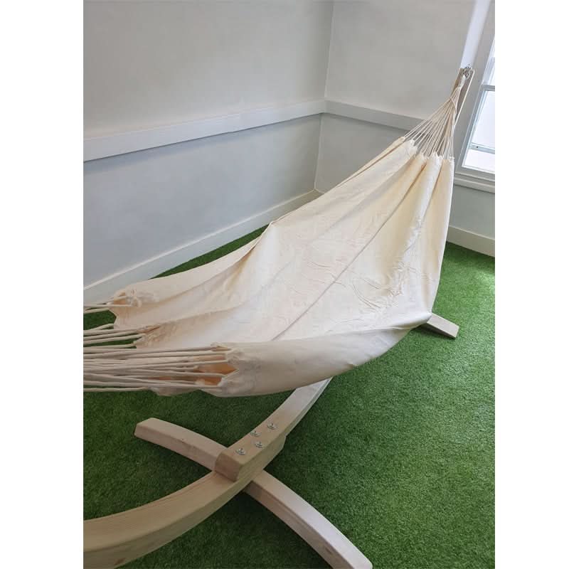 Beige hammock on a wooden stand in a room with green carpet and white walls.