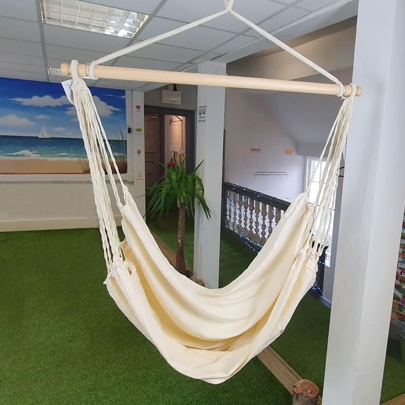 Beige hammock hanging indoors on a white stand with a scenic wall mural in the background.