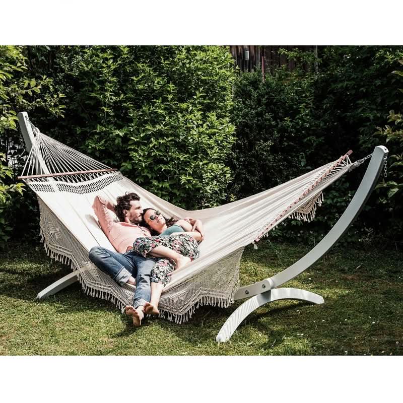 Two people relaxing in a hammock with a white stand in a garden setting.
