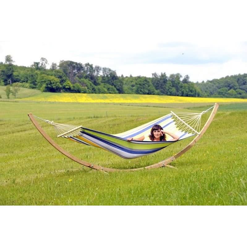 Person in a striped hammock in a grassy field with trees and flowers in the background