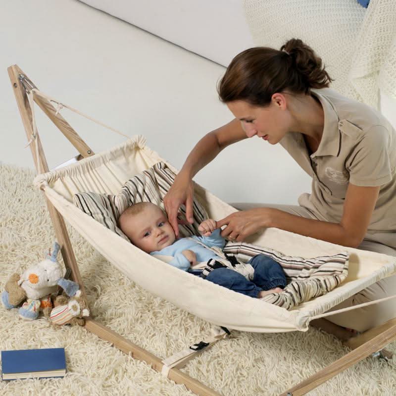 Woman adjusting a baby in a hammock with a neutral background