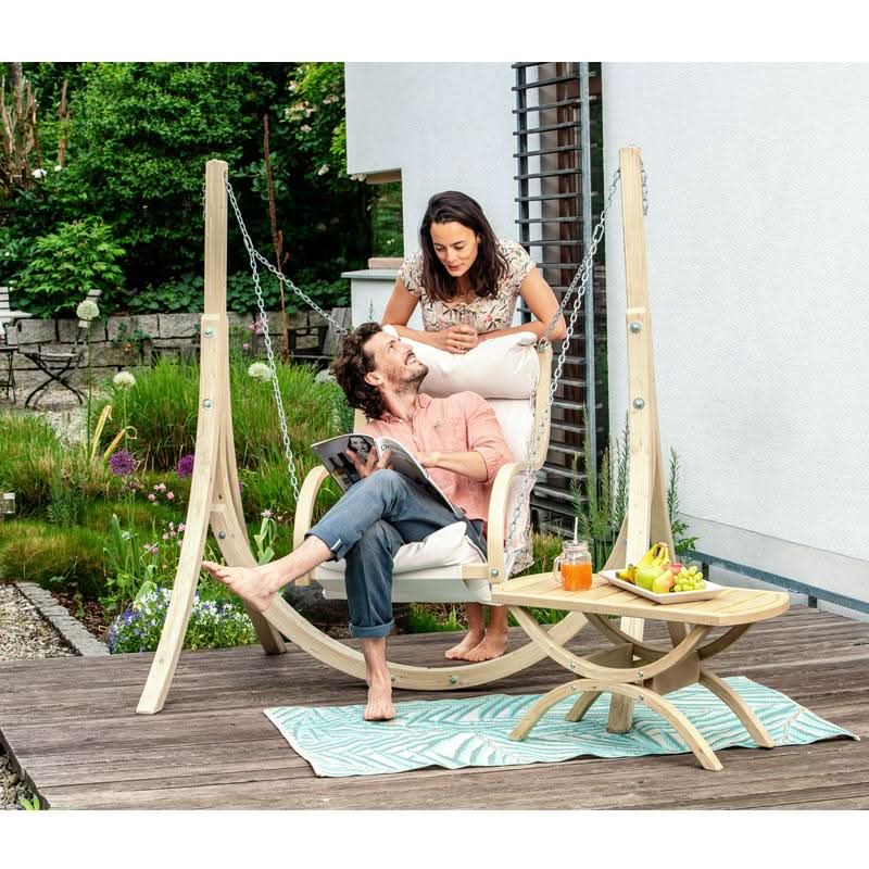 A couple in a hanging chair on a wooden deck with a garden view
