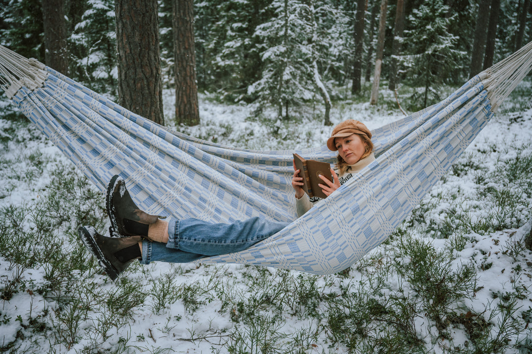 Woman sat on hammock hanging in the woods in winter