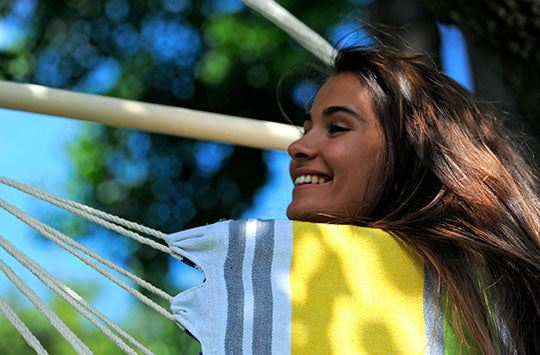 A woman smiling while sitting in a yellow, blue and green striped hammock