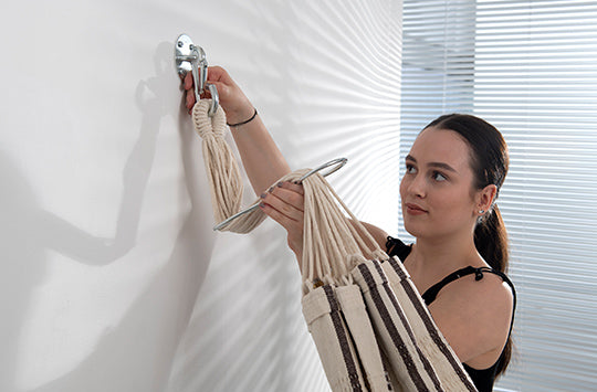 A woman using a hammock Angel length adjuster to shorten her hammock on the wall