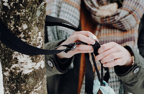 A person securing their hammock to a tree with a hammock fixing. 