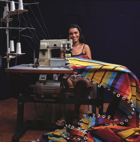 A woman sitting at a sewing machine with colourful fabric around her