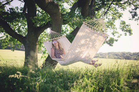 Person relaxing in a hammock under a tree in a field