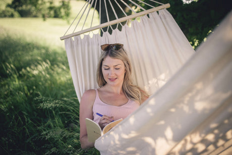 Woman reading a book in a white hammock in a grassy outdoor setting